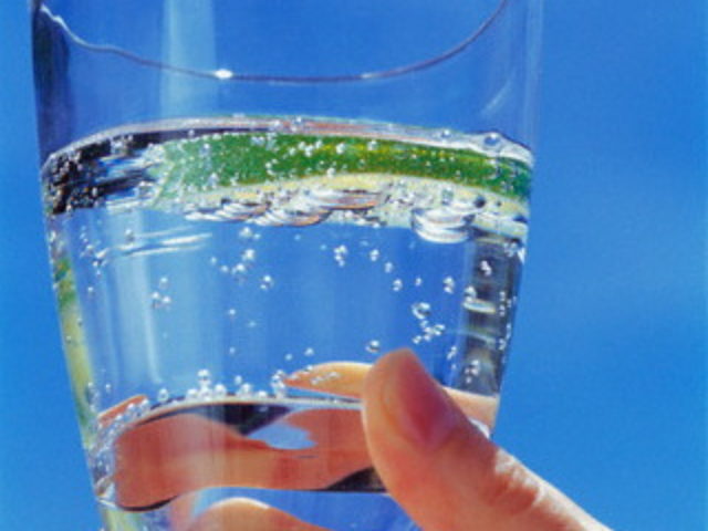 Hand holding glass of sparkling water with lime slice