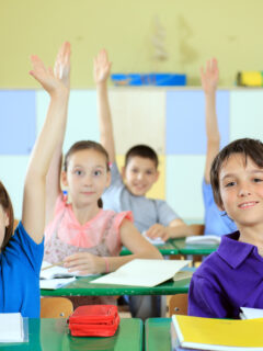 Elementary-school-students-raising-hands-in-classroom_
