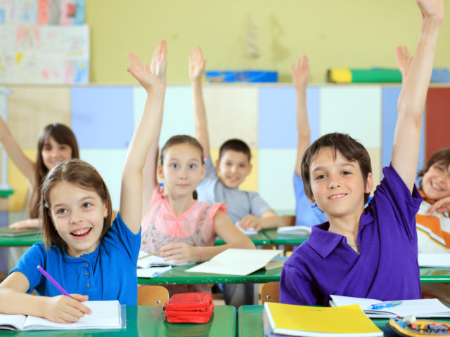 Elementary-school-students-raising-hands-in-classroom_