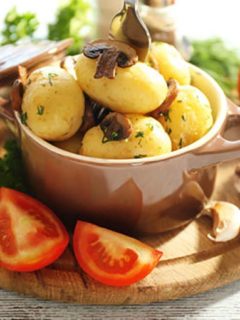 Young boiled potatoes in pan with vegetables on table in kitchen