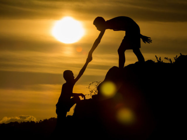 Silhouette of  helping hand of a friend with flare light.